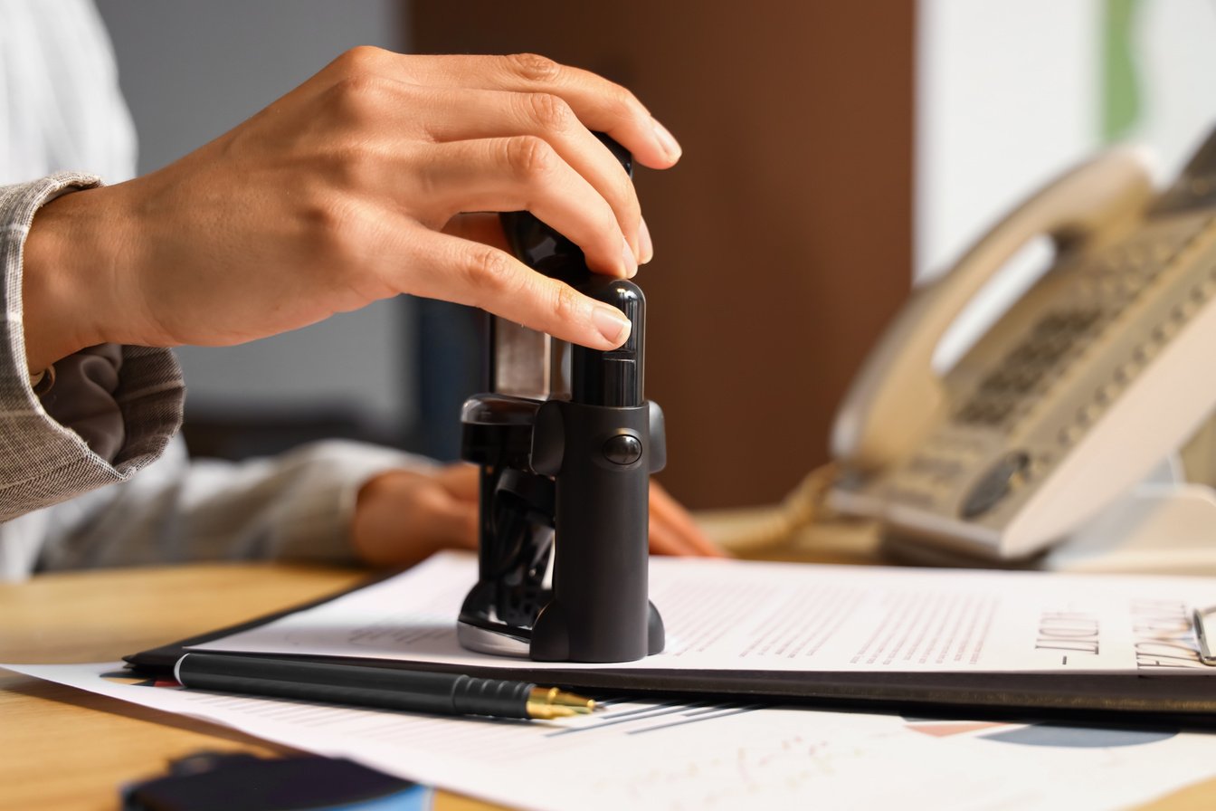 Female Notary Public Attaching Seal to Document in Office, Closeup